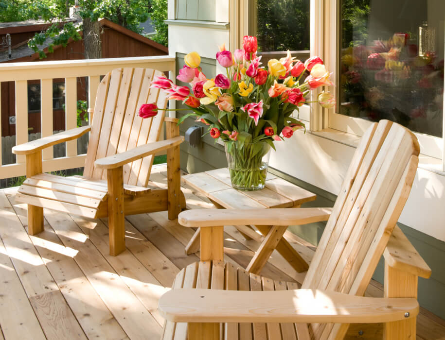A sunny porch with wooden chairs and a vase of flowers