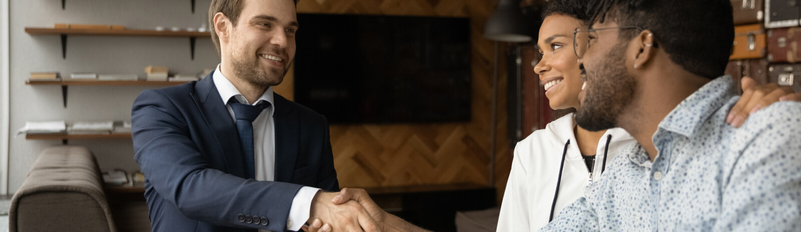 Man in suit talking with a couple, both men are shaking hands