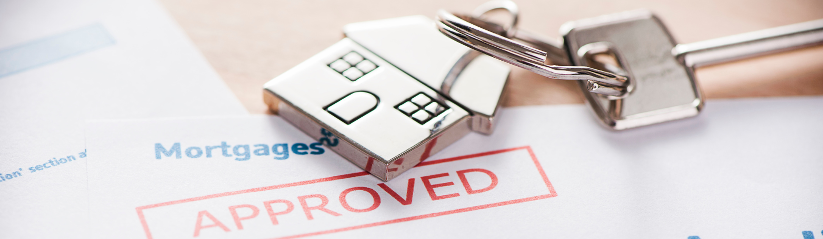 Mortgage approval document stamped 'APPROVED' with house keychain and keys, symbolizing successful home loan and homeownership.