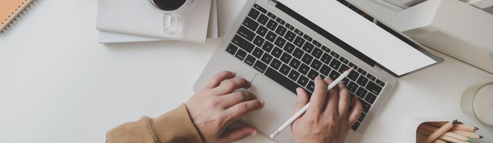 man typing on a laptop holding a pencil